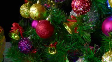 Siyah arka planda, Noel topları olan bir vazo süslü bir Noel ağacının yanında dönüyor.