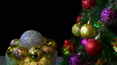 Siyah arka planda, Noel topları olan bir vazo süslü bir Noel ağacının yanında dönüyor.