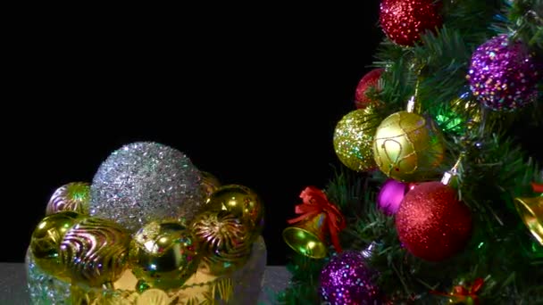在黑色的背景上 一个装有圣诞球的花瓶在一棵装饰过的圣诞树旁旋转着 — 图库视频影像