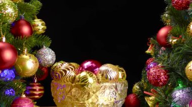 Siyah arka planda, Noel topları olan bir vazo süslenmiş Noel ağaçlarının yanında dönüyor.