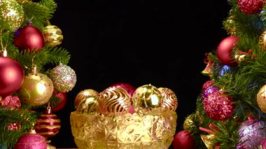 Siyah arka planda, Noel topları olan bir vazo süslenmiş Noel ağaçlarının yanında dönüyor.
