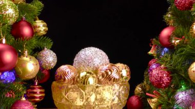 Siyah arka planda, Noel topları olan bir vazo süslenmiş Noel ağaçlarının yanında dönüyor.