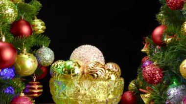 Siyah arka planda, Noel topları olan bir vazo süslenmiş Noel ağaçlarının yanında dönüyor.