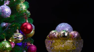 Siyah arka planda, Noel topları olan bir vazo süslü bir Noel ağacının yanında dönüyor.
