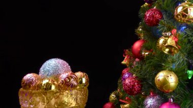 Siyah arka planda, Noel topları olan bir vazo süslü bir Noel ağacının yanında dönüyor.