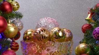 Gümüş arka planda, Noel topları olan bir vazo süslenmiş Noel ağaçlarının yanında dönüyor.