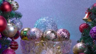 Gümüş arka planda, Noel topları olan bir vazo süslenmiş Noel ağaçlarının yanında dönüyor.