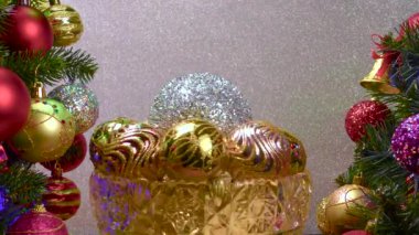 Gümüş arka planda, Noel topları olan bir vazo süslenmiş Noel ağaçlarının yanında dönüyor.