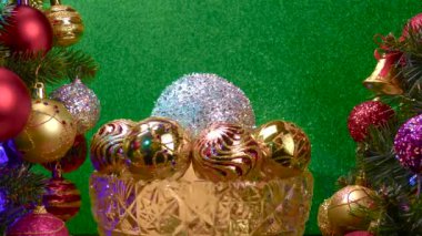 Yeşil arka planda, Noel topları olan bir vazo süslenmiş Noel ağaçlarının yanında dönüyor.