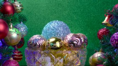 Yeşil arka planda, Noel topları olan bir vazo süslenmiş Noel ağaçlarının yanında dönüyor.