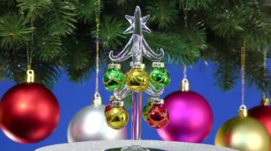 Mavi arka planda, küçük bir Noel ağacı Noel toplarıyla süslenmiş dönen büyük bir Noel ağacının yanında döner.