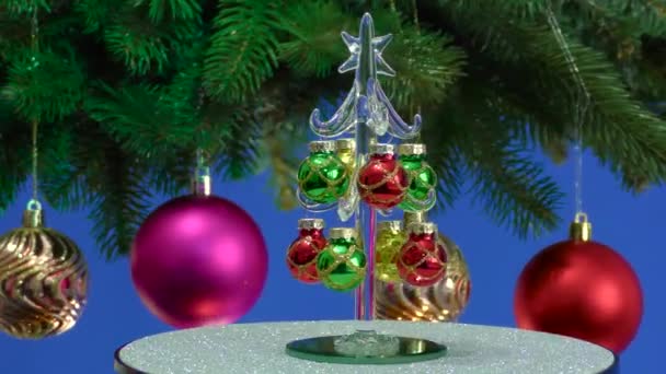 在蓝色的背景上 一棵小圣诞树在一棵旋转的大圣诞树旁边旋转 圣诞树上装饰着圣诞球 — 图库视频影像