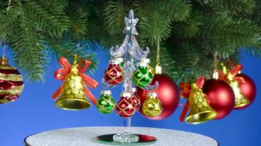 Mavi arka planda, küçük bir Noel ağacı Noel topları ve çanları ile süslenmiş dönen büyük bir Noel ağacının yanında döner.