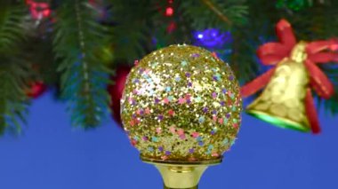 Mavi arka planda, Noel balosu Noel topları ve çanları ile süslenmiş dönen büyük bir Noel ağacının yanında döner.