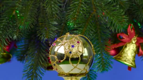 在蓝色的背景下 圣诞球在旋转的大圣诞树附近旋转 圣诞树上装饰着圣诞球和圣诞钟声 — 图库视频影像