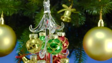 Mavi arka planda, Noel ağacı dallarının yanında, küçük bir Noel ağacı gri bir stantta dönüyor.