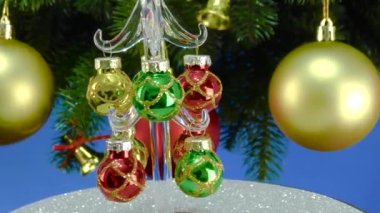 Mavi arka planda, Noel ağacı dallarının yanında, küçük bir Noel ağacı gri bir stantta dönüyor.