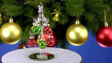 Mavi arka planda, Noel ağacı dallarının yanında, küçük bir Noel ağacı gri bir stantta dönüyor.