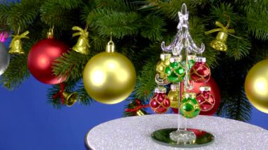 Mavi arka planda, Noel ağacı dallarının yanında, küçük bir Noel ağacı gri bir stantta dönüyor.