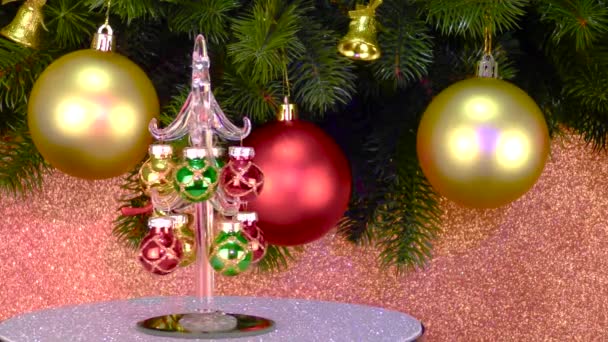 在粉红的背景上 靠近有圣诞装饰品的圣诞树枝头 一棵小小的圣诞树在灰色的看台上旋转着 — 图库视频影像