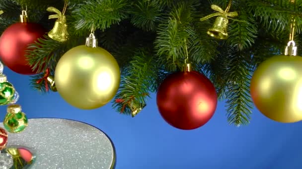 Auf Blauem Grund Der Nähe Der Weihnachtsbaumzweige Mit Weihnachtsschmuck Dreht — Stockvideo