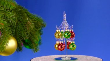 Büyük süslü Noel ağacı dallarının yanında küçük bir Noel ağacı mavi bir zemin üzerinde döner.