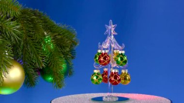 Büyük süslü Noel ağacı dallarının yanında, bir Noel topu mavi arka planda döner.