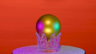 Kırmızı arka planda, Noel topu gümüş bir stantta döner.