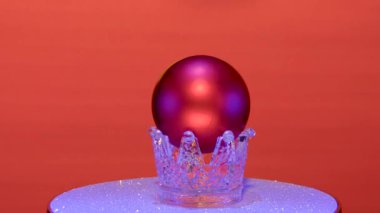 Kırmızı arka planda, Noel topu gümüş bir stantta döner.