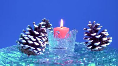 Mavi arka planda, Noel konileri ve bir mum cam yüzeyde döner.