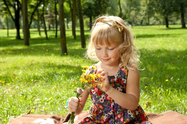 Kleines Mädchen mit Blumen im Park — Stockfoto