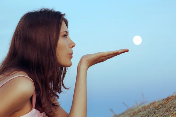 Beautiful brunette blows the moon with palm — Stock Photo, Image