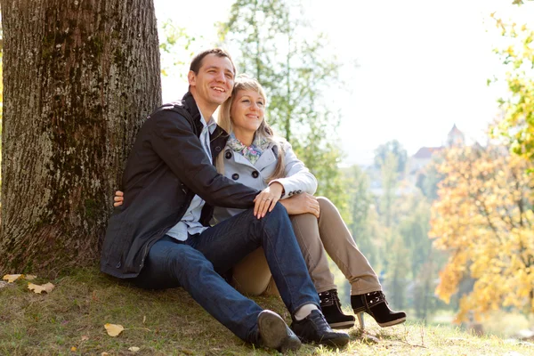 Szerető fiatal pár ül a földön, fa — Stock Fotó