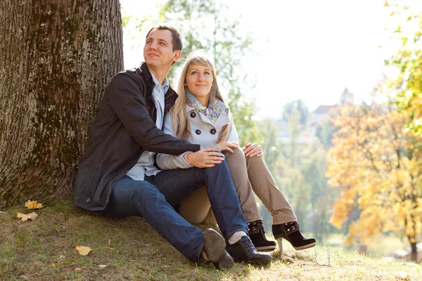 Young loving couple sitting on ground by tree — Stock Photo, Image