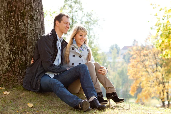 Joven pareja amorosa sentada en el suelo por árbol Fotos de stock libres de derechos