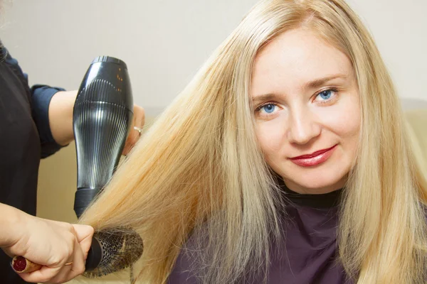 Hairdressers hands drying long blond hair — Stock Photo, Image