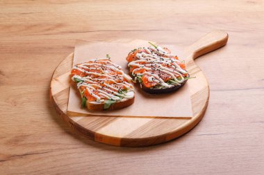 Sağlıklı kahvaltı için yuvarlak ahşap tepside füme ve tuzlu somon, roka ve sos ile iki sandviç..