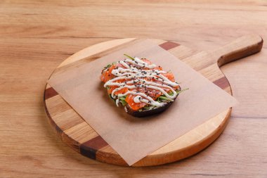 Sağlıklı kahvaltı için füme ve tuzlu somon, roka ve soslu sandviç yuvarlak ahşap tepside..