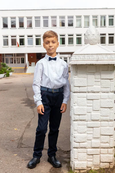 校庭には 制服を着た美しい8歳の男の子 黒いズボン 蝶ネクタイの白いシャツがポーズをとっています — ストック写真
