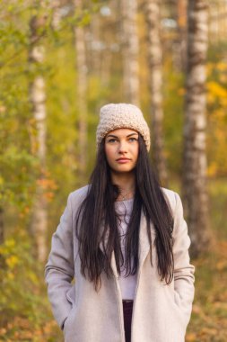 Sonbahar parkında eğlenen neşeli genç bir kadının portresi. Güz gri ceketli ve örgü şapkalı güzel esmer kız. Doğada rahatla..