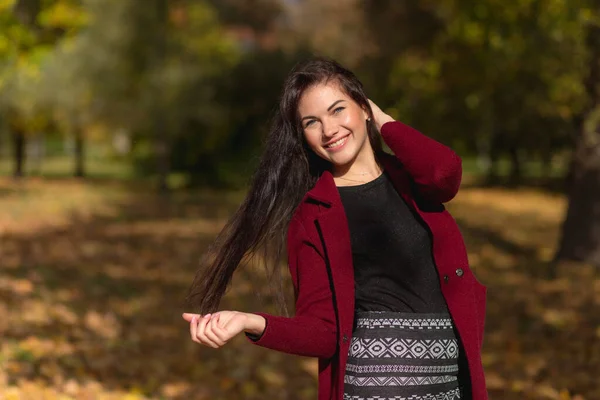 一个快乐的年轻女子在秋天的公园里享受的画像 美丽的黑发姑娘 穿着秋天的红色外套和黑色毛衣 放松的天性 高质量的照片 — 图库照片