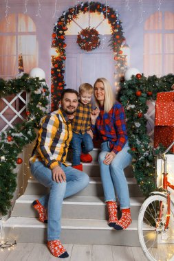 Dekoratif verandada poz veren mutlu bir aile. Evde Noel kutlaması. Anne, baba ve oğul rahat giyindi. Mutlu aile eğlencesi onların evinde oynuyor. Noel dekore edilmiş ev içi