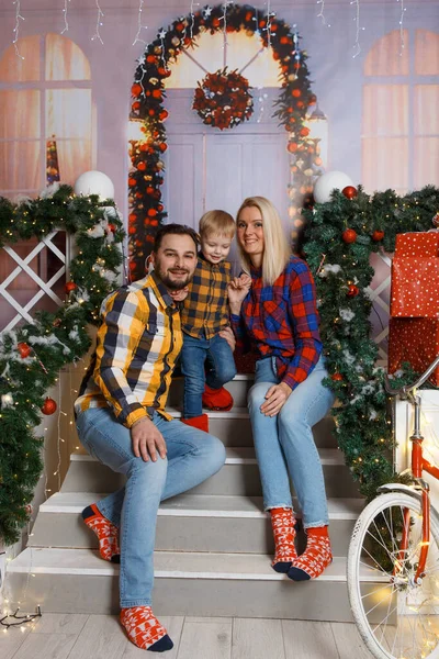 Happy family posing on a decorative porch . Christmas celebration at home. Mom, Dad and son weared in casual. Happy family funny playing in their house. Christmas decorated home interior