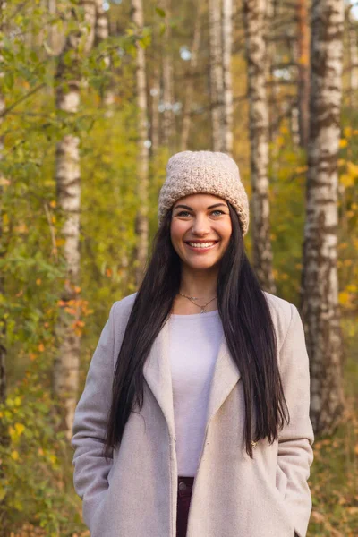 Sonbahar parkında eğlenen neşeli genç bir kadının portresi. Güz gri ceketli ve örgü şapkalı güzel esmer kız. Doğada rahatla..