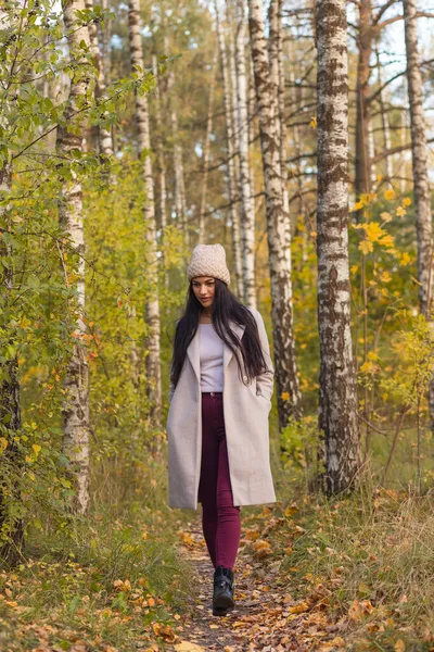 Sonbahar parkında eğlenen neşeli genç bir kadının portresi. Güz gri ceketli ve örgü şapkalı güzel esmer kız. Doğada rahatla..