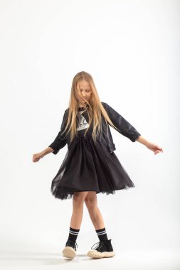 Dans eden, uzun kahverengi saçlı, holigan tarzı giyinmiş, beyaz arka planda dans eden genç bir kızın tam boy portresi..