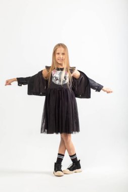 Dans eden, uzun kahverengi saçlı, holigan tarzı giyinmiş, beyaz arka planda dans eden genç bir kızın tam boy portresi..
