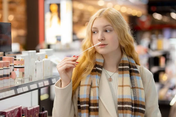 美丽的年轻女子 一头长长的金发 嗅着吸墨机 在商店里选择香水 为你自己寻找一种芬芳 或作为礼物送给你爱的人 — 图库照片