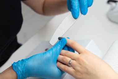 Güzellik salonundaki usta kıza manikür yaptırıyor. Usta elinde bir dosya ile çivileri dosyalar..