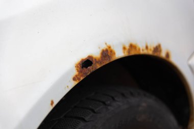 Beyaz eski arabanın yan tarafında pas var. Eski, yıpranmış metal yüzeydeki pas deliği..